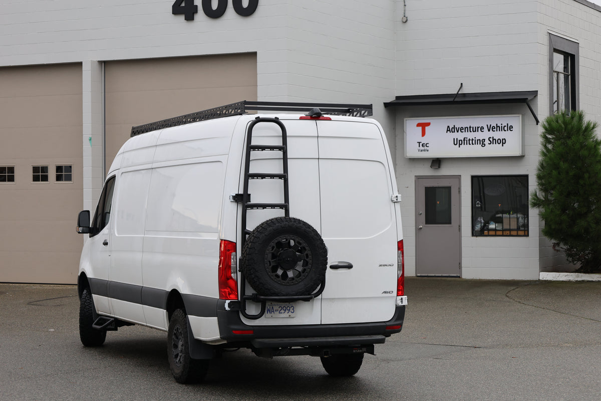 Tec Vanlife tire ladder carrier installed on the rear door of a white Sprinter outside the Tec Vanlife shop